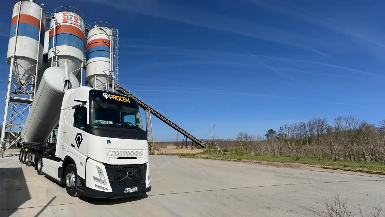Ciągnik siodłowy Volvo z naczepą SILO przy węźle betoniarskim, w tle silosy cementu