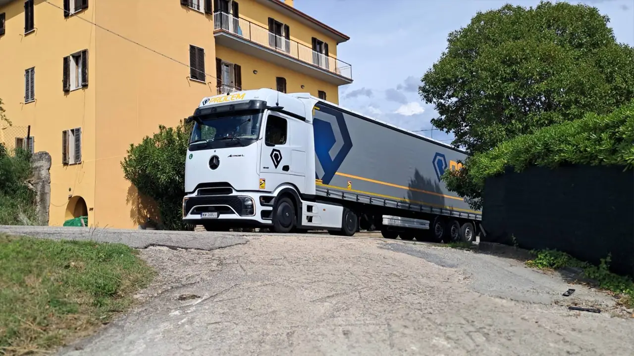 Zestaw Mercedes-Benz z naczepą plandekową w barwach PROCEM na wąskiej ulicy w zabudowie miejskiej